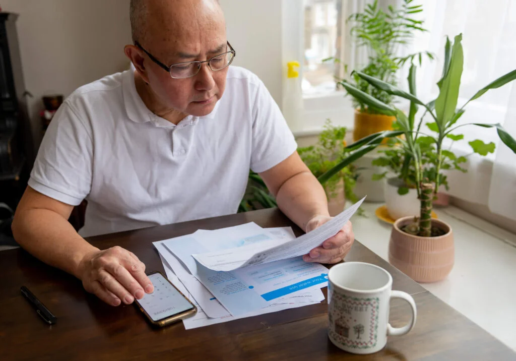 A senior man sitting by a table calculating the raising cost of energy and tax bills. Inflation and living cost