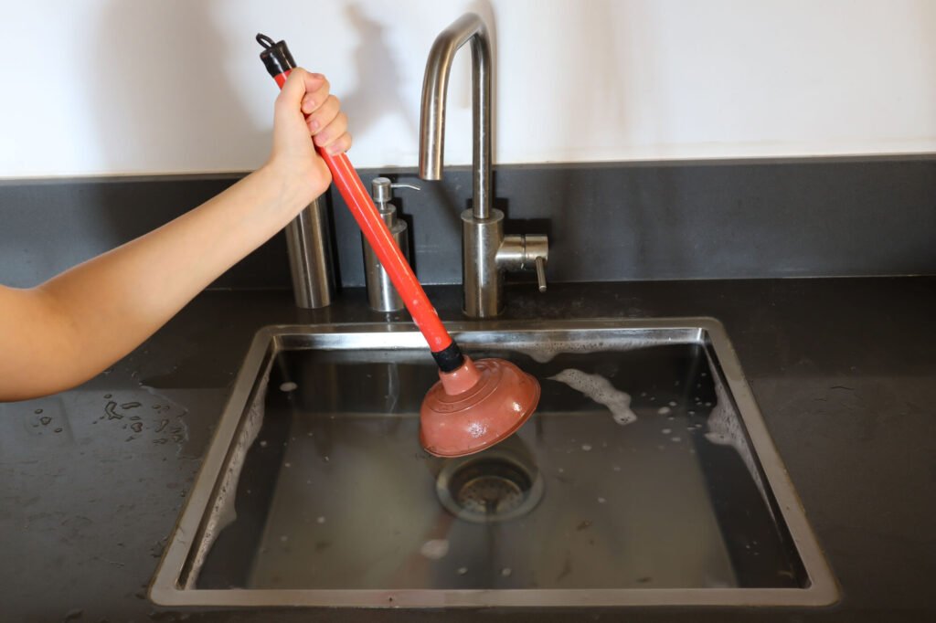 plumber using a plunger to clear blocked sink full of water