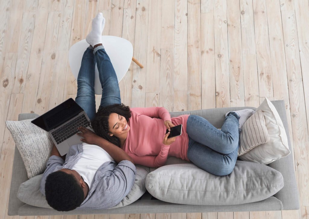 Young African American Couple Relaxing At Home With Laptop And Smartphone