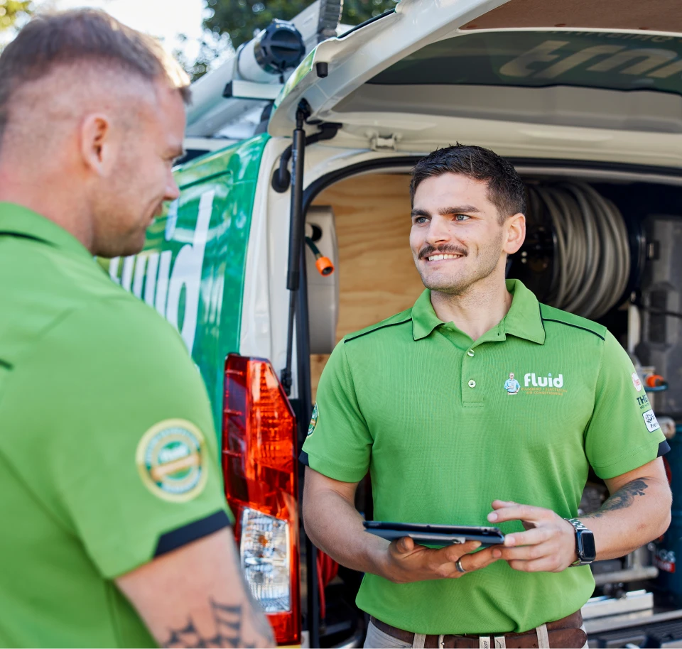 Fluid technicians discussing a service job beside a branded van, with one technician holding a tablet.