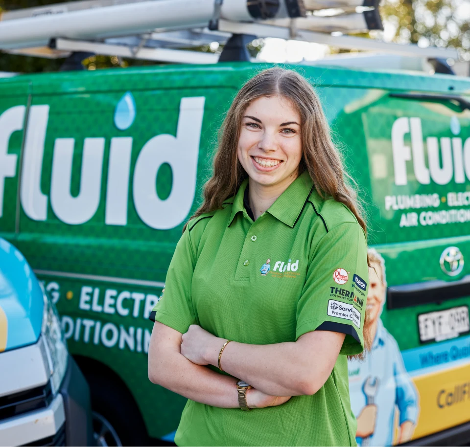 Smiling Fluid team member in a green polo shirt standing with arms crossed in front of a branded service van.