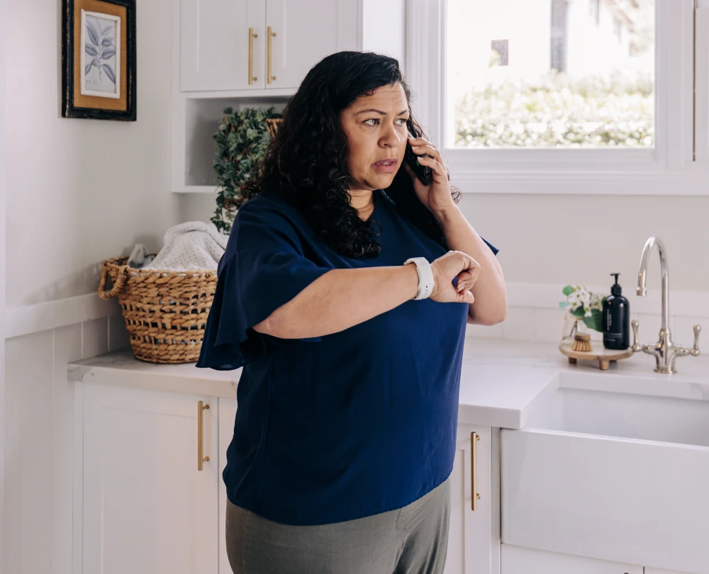 Homeowner checking her smartwatch while speaking on the phone in a bright kitchen.