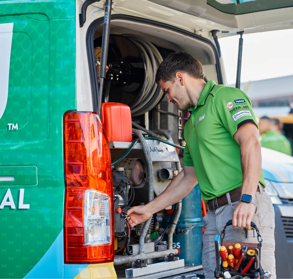 Fluid technician checking equipment inside a branded service van while holding a tool bag.