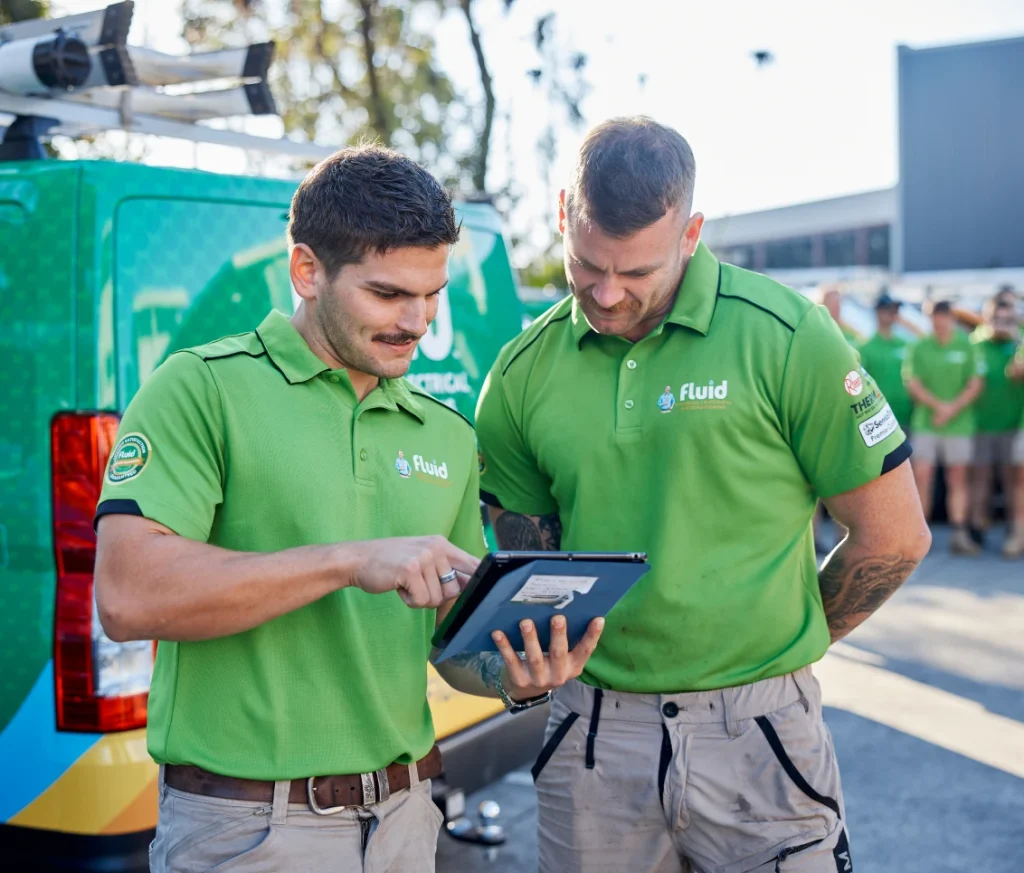 Two Fluid technicians reviewing job details on a tablet beside a branded service van.
