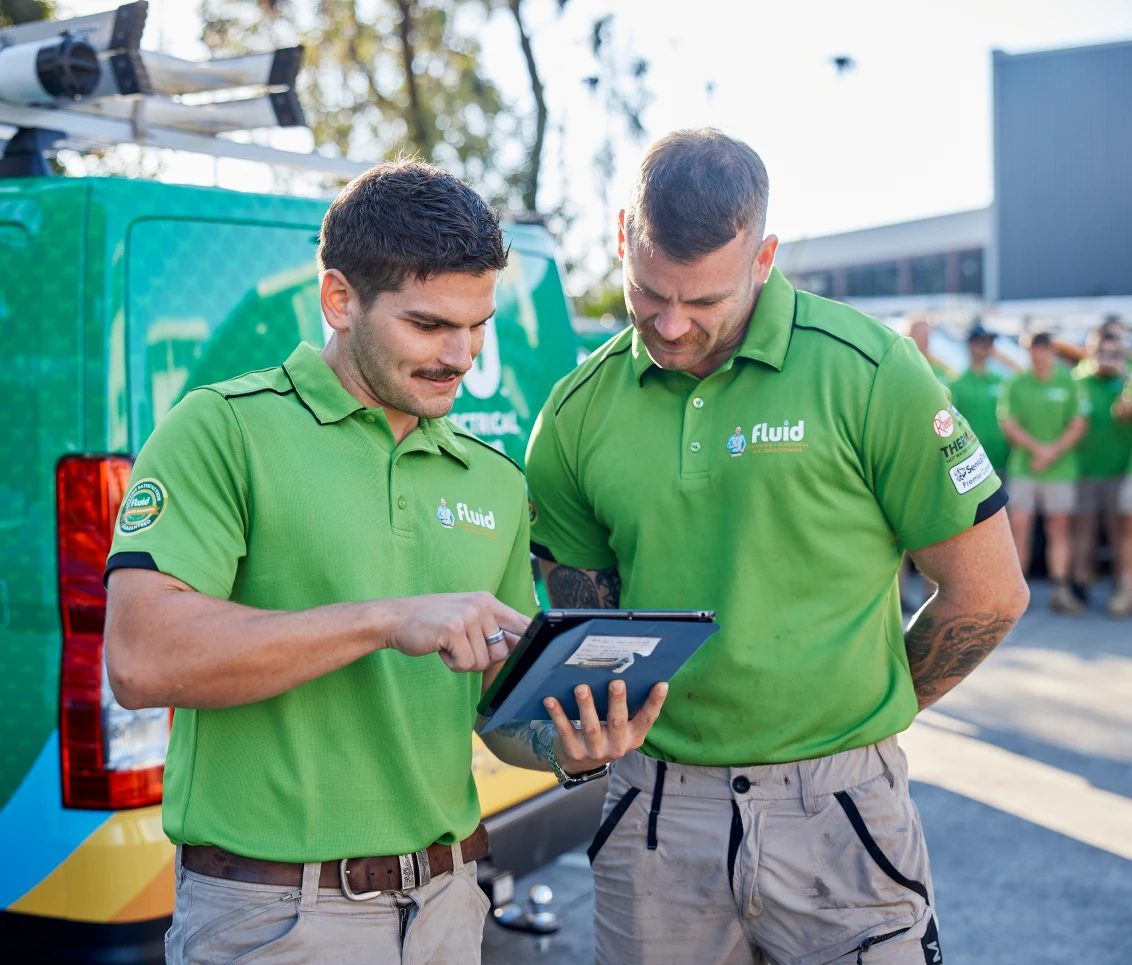 Two Fluid technicians reviewing job details on a tablet beside a branded service van.