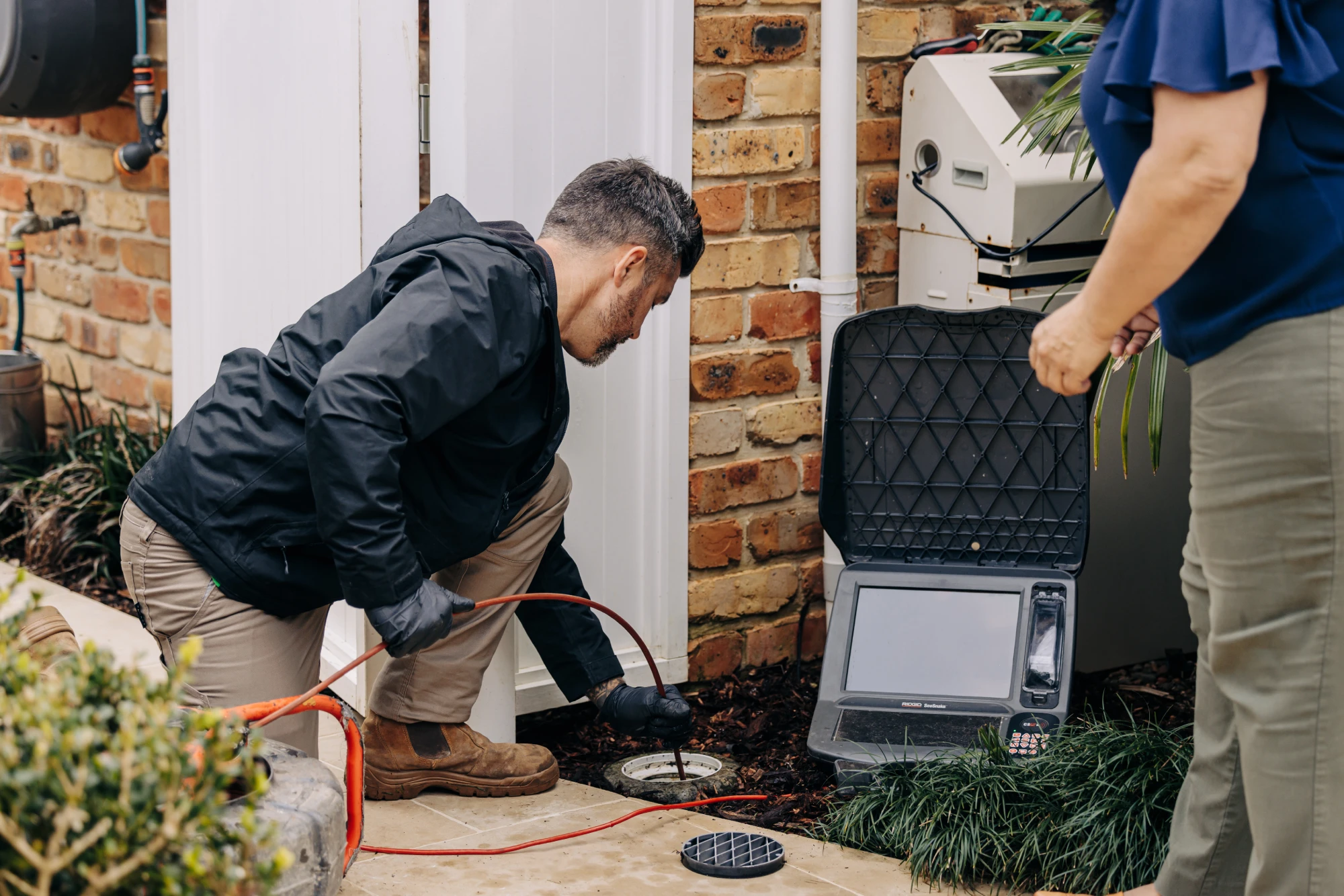 Fluid technician inspecting an outdoor drain at a residential property using diagnostic equipment.