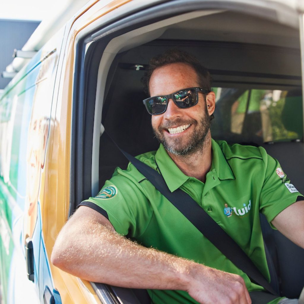 Smiling Fluid team member wearing a green polo shirt while seated in a branded service van.