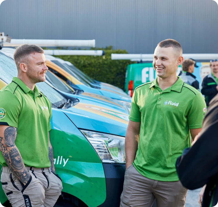 Two Fluid technicians in green polo shirts talking beside branded service vans.