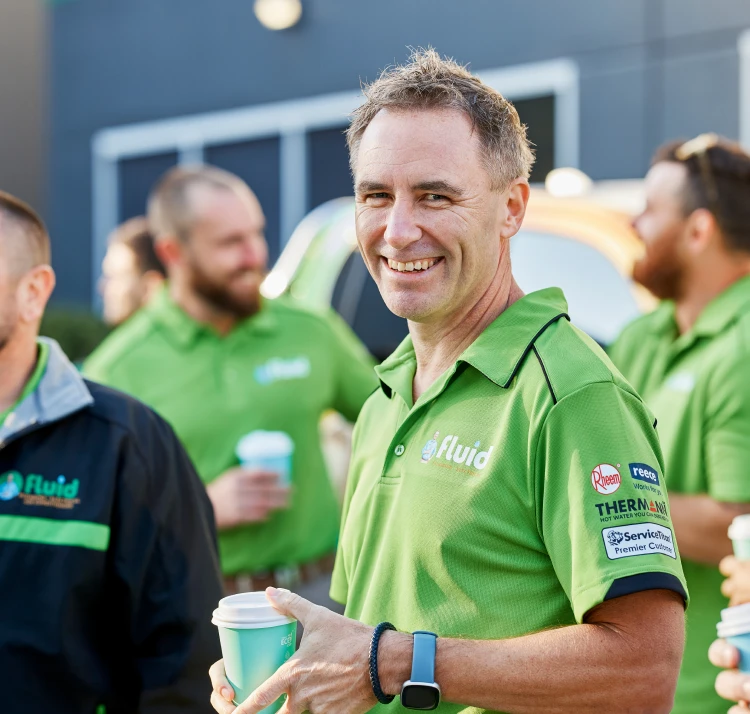 Smiling Fluid team member holding a coffee cup during an outdoor team gathering near branded service vehicles.