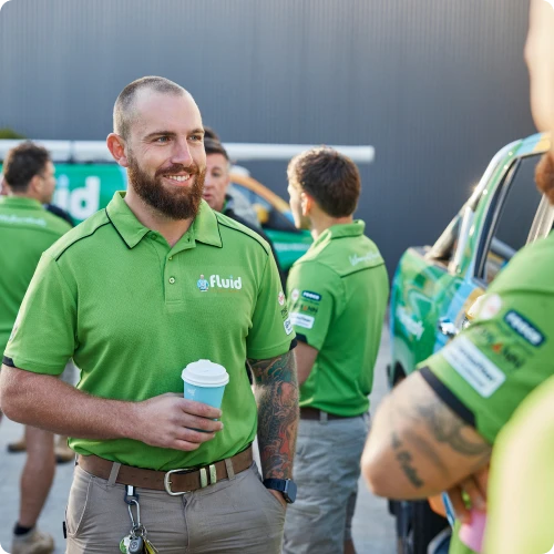 Fluid technician holding a coffee cup while standing with the team near a branded service van.